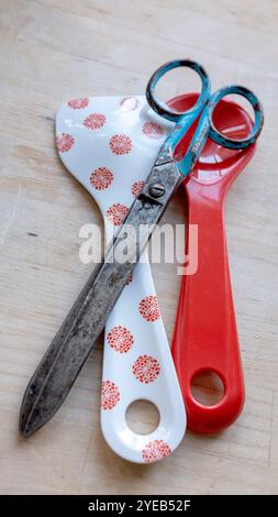 A pair of old rusty, metal, vintage scissors with a new plastic pair of salad servers. New versus old. Modern and old together. Stock Photo