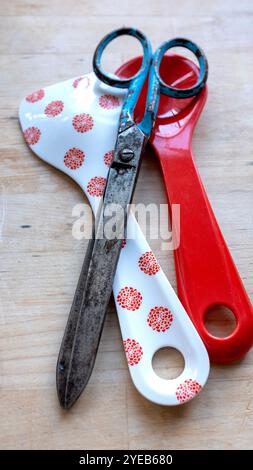 A pair of old rusty, metal, vintage scissors with a new plastic pair of salad servers. New versus old. Modern and old together. Stock Photo