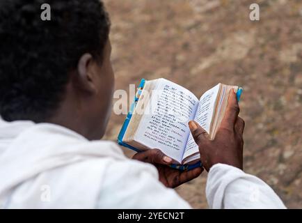 Young man reading his prayer book written in Amharic language on a Sunday morning. Lalibela, Ethiopia Stock Photo