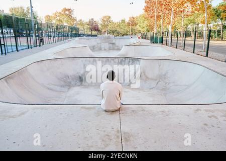 unrecognizable man sitting on a ramp thinking while looking at a vacant skatepark Stock Photo