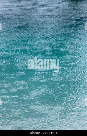 raindrops falling on a swimming pool creating abstract pattern suitable for use as a backdrop or background Stock Photo