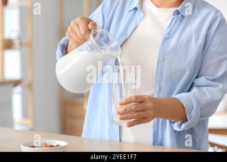 Beautiful senior woman pouring milk from jug into glass in kitchen, closeup Stock Photo