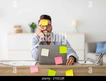 A lot of work concept. Tired freelancer man sleeping at workplace with stickers on foehead and computer Stock Photo