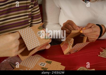 Two people assembling decorative gingerbread house boxes. One person holds a partially assembled box while the other is attaching a piece. The setting Stock Photo