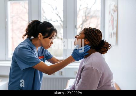 Focused female medical expert checking lymph nodes of young patient in examination room at hospital Stock Photo