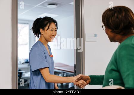 Smiling female medical professional greeting senior patient while standing at doorway of examination room Stock Photo