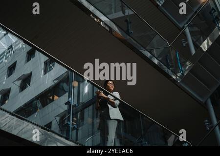 Low angle view of businesswoman with smart phone standing by glass railing Stock Photo