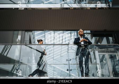 Low angle view of businesswoman walking by businessman standing at glass railing Stock Photo
