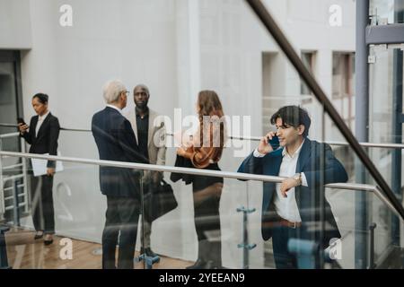 Young businessman talking on smart phone by male and female colleagues discussing at lobby Stock Photo