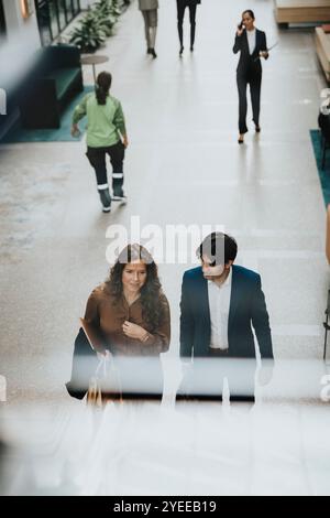 Mature businesswoman discussing with young male colleague while walking at lobby Stock Photo