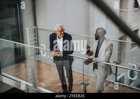 Smiling businessmen discussing while standing by glass railing Stock Photo
