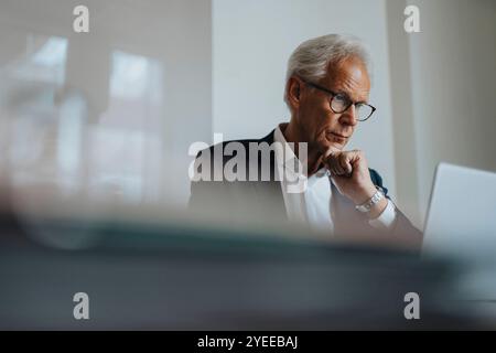 Businessman wearing eyeglasses with hand on chin working at office Stock Photo