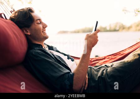 Side view of smiling man using smart phone while lying down in hammock Stock Photo