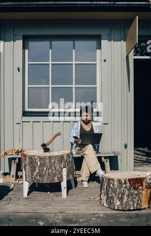 Female designer using laptop while sitting on bench outside workshop Stock Photo