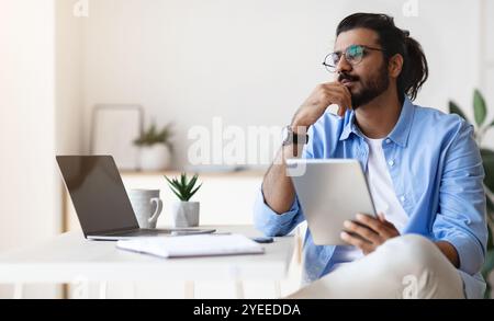Pensive Young Arab Male Freelancer Using Gigital Tablet And Daydreaming At Home Stock Photo