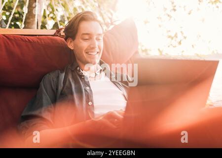 Smiling young man using laptop sitting in hammock Stock Photo