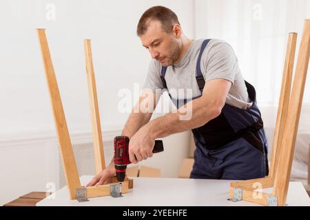 Male Carpenter Using Electric Drill Assembling Wooden Table In Studio Stock Photo