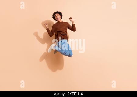 Joyful african american young man in casual outfit jump against beige background, expressing excitement energy for advertising promotions Stock Photo
