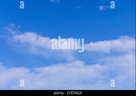 Soft white clouds float leisurely across a vibrant blue sky under the warm sun. Stock Photo