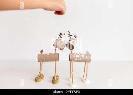 Hand holding wooden stick controlling DIY reindeer puppets crafted from recycle toilet paper roll cardboard tubes and bottle caps. Minimalistic shot f Stock Photo