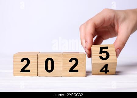 2025 New Year. Woman turning wooden cube on white table, closeup Stock Photo