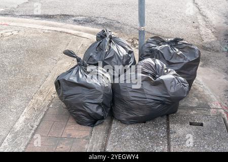 Front view of garbage in black plastic bag at garbage dump on roadside or footpath is in downtown area. Stock Photo