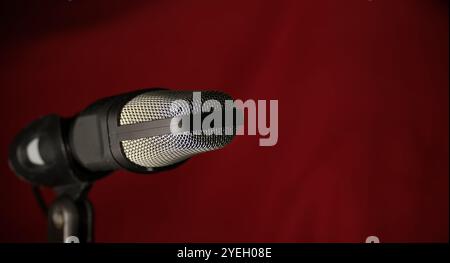 Professional studio microphone with metal mesh grille against dark red background, ideal for music recording, podcasting, and broadcasting Stock Photo