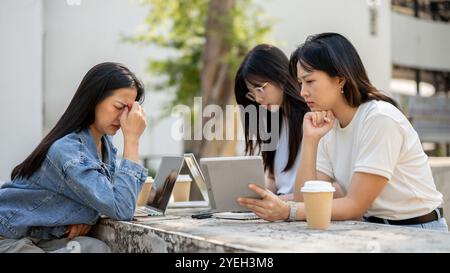 A group of serious, stressed young Asian female college students is working together, looking concerned about their project as they work on their lapt Stock Photo