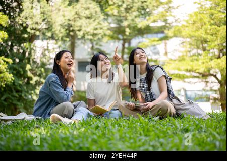 A group of cheerful Asian female college students sits together on the grass in their college park, enjoying a lively conversation. education, friends Stock Photo