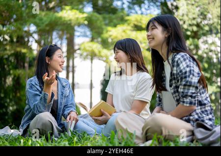 A group of cheerful Asian female college students sits together on the grass in their college park, enjoying a lively conversation. education, friends Stock Photo