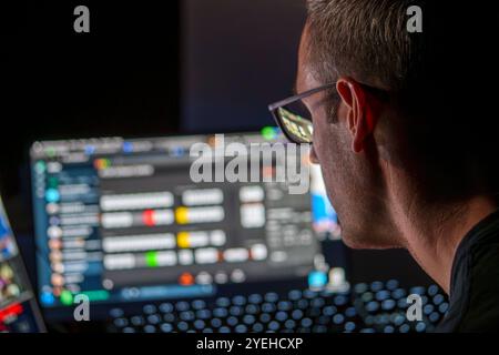 Cybersecurity Professional Analyzing Data on Multiple Screens in a Low-Light Workspace for Network Security Assessment Stock Photo