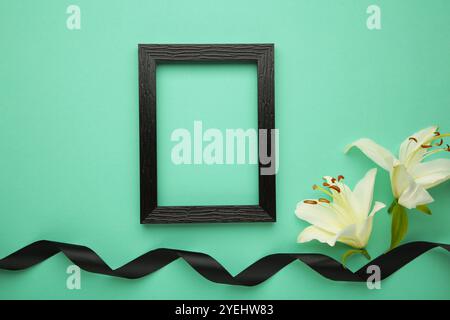 Beautiful lily flower with blank frame and black funeral ribbon on mint background. Stock Photo