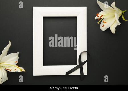 Beautiful lily flower with blank frame and black funeral ribbon on black background. Stock Photo