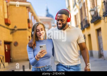 Multiracial happy couple walking in the city using mobile phone and headphones Stock Photo