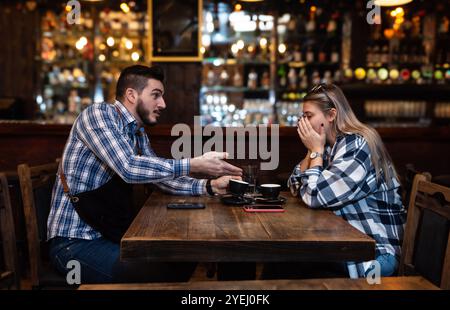Bartender life. Two young bartenders argue about coffee taste and shifts in the workplace. Employees waiters in the bar, mad and woman, fight and misu Stock Photo