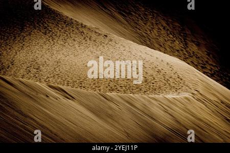 Golden sand dune with textured surface, illuminated by light and shadow in an arid desert landscape Stock Photo