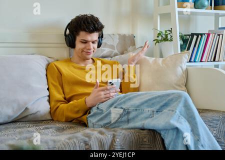 Young guy 19-20 years old in headphones using smartphone, talking on video call Stock Photo