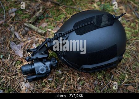 Black tactical military equipment, helmet with night vision device lies on the grass. Close up. Stock Photo