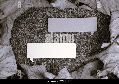 Two speech bubbles against a grass background surrounded by dry leaves in a black and white image. Stock Photo