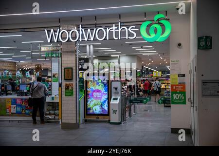 Exterior view of a Woolworths store entrance inside a shopping mall, with visible branding, promotional posters, and customers inside the store. Stock Photo