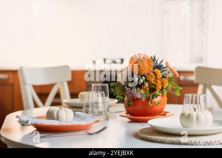 Thanksgiving day table setting decoration beautiful centerpieces with orange flowers in pumpkins on white table in home kitchen interior. Close up. Stock Photo
