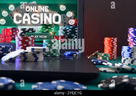 Concept of playing online casino games with laptop with gaming application on plush green mat and stacks of chips on top and around. Front view. Stock Photo