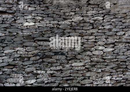 Stone wall made of stacked flat stones arranged horizontally. The stones fit snugly against each other. Stock Photo