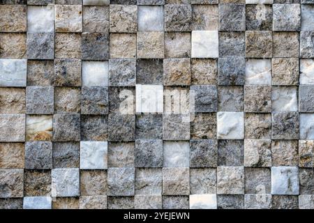 Wall made up of small square tiles arranged in a grid pattern. The tiles vary in color and texture, with shades of gray, beige, and white. Stock Photo