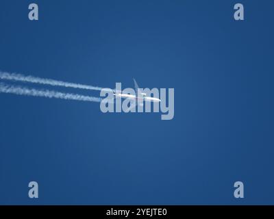 Tele view of Emirates jet airliner flying at high altitude in blue sky with contrails Stock Photo