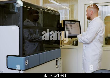 Male technician using advanced laboratory machinery for scientific research, touching digital screen for data input, standing in modern laboratory environment Stock Photo