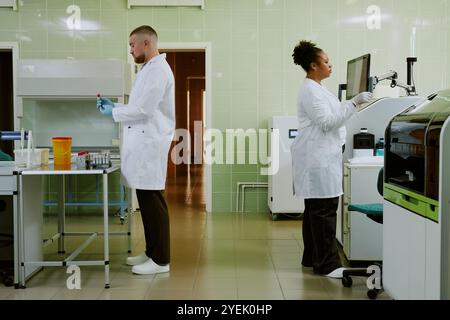 Scientists conducting research in modern laboratory setting, both wearing lab coats and working with various equipment while engaged in scientific tasks Stock Photo