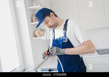Dedicated young handyman skillfully performing plumbing tasks during a home renovation in a bright kitchen setting Stock Photo