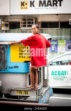 A young Filipino many holds on to the back of a jeepney bus speeding through Manila City, The Philippines. Stock Photo