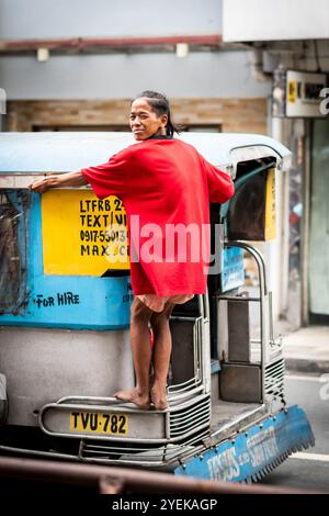 A young Filipino many holds on to the back of a jeepney bus speeding through Manila City, The Philippines. Stock Photo